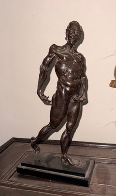 une statue en bronze représentant un homme en train de courir, posée sur un socle en marbre