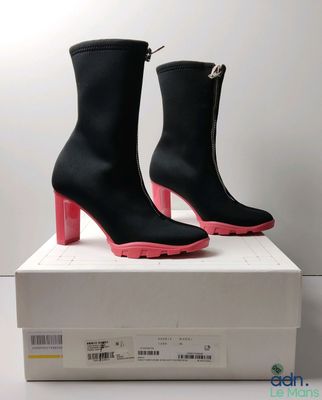 une paire de bottes noires aux semelles roses posée sur une boîte