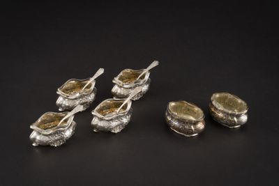 six cuillères en argent avec leurs repose-cuillères, posées sur un support noir