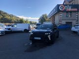 La voiture noire est garée devant l'immeuble, à côté d'autres voitures.