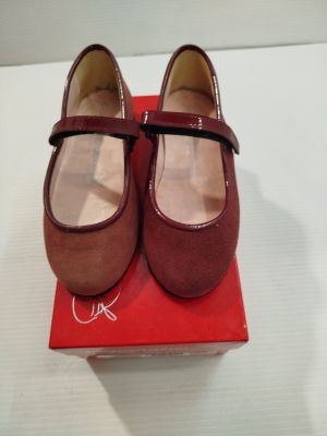 une paire de chaussures rouges posée sur une boîte rouge, elle-même posée sur une surface blanche