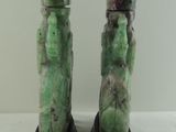 pair of green jade figurines sitting on a wooden stand