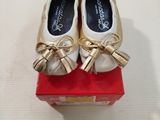 une paire de chaussures blanches et dorées ornées de nœuds, posée sur une boîte rouge