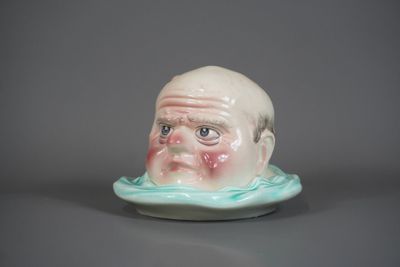 une petite figurine en céramique représentant un homme dont le visage est sculpté sur une soucoupe