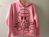 un sweat à capuche rose avec un chat dessiné dessus, accroché au mur