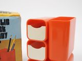 an orange desk organizer with three drawers next to a box of pencils