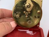 a person holding a red case with a gold clock inside of it