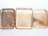 trois petits plateaux en métal posés les uns à côté des autres sur une surface blanche