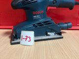 une ponceuse orbitale Bosch posée sur une table, à côté d'une boîte rouge