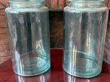 deux bocaux en verre posés sur une table, avec un mur de briques en arrière-plan