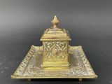 an antique brass inkwell on a tray on a black background