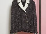 une veste en tweed noir et blanc suspendue à un cintre devant un mur rose et blanc