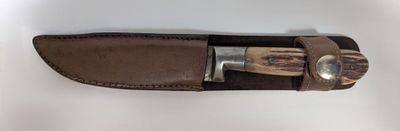 brown leather sheath with a knife on top of it on a white surface