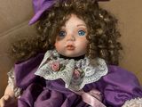 doll in a box wearing a purple dress and a purple bow