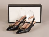 une paire de chaussures en cuir noir avec des boucles dorées et une boîte noire