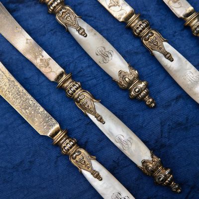 six antique silverplated knives on a blue cloth with a blue background
