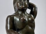 bronze statue of a woman sitting on a rock with her hand on her head