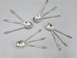 six cuillères en argent sont disposées en cercle sur une table