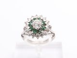 a close up of a diamond and emerald ring on a white surface