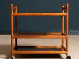 a wooden trolley with three shelves on wheels on a floor