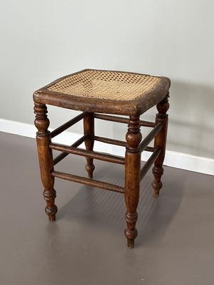 un vieux tabouret en bois avec une assise en osier, posé sur un sol gris