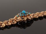 a gold bracelet with turquoise stones on a black surface