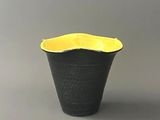 un vase noir et jaune posé sur une surface grise