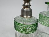 two glass bottles with green designs on them on a white surface