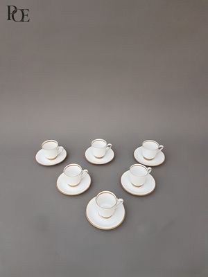 un service de six tasses à café blanches avec leurs soucoupes, posé sur un support gris