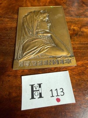 une plaque en laiton représentant une femme portant un foulard, posée sur une table à côté d'un autocollant