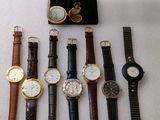 plusieurs montres différentes et un présentoir à montres posés sur une surface blanche