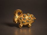 une photo représentant une figurine de bélier en or et en turquoise posée sur une table