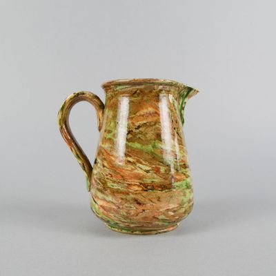a brown and green vase with a handle on a table