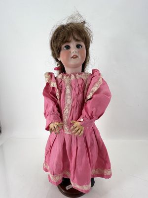 une poupée à l'ancienne, avec une robe rose et des cheveux bruns