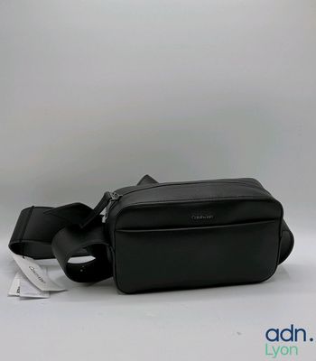 sac banane en cuir noir avec une lanière noire et une étiquette blanche sur le côté