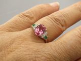 Quelqu'un tient dans sa main une bague sertie d'un diamant rose et d'une émeraude.
