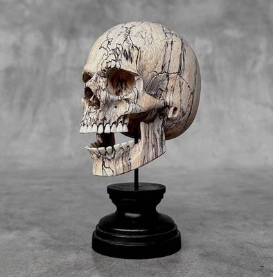 a wooden skull on a black stand with a gray background