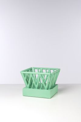 un panier vert posé sur une table près d'un mur blanc