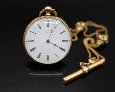 une montre de poche en or avec une clé, posée sur un fond noir