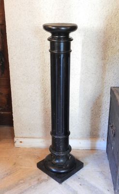 a black pedestal with a wooden base in the corner of a room
