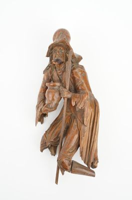 statue en bois représentant un homme muni d'un bâton et portant un chapeau, sur fond blanc