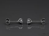 a pair of diamond stud earrings on a reflective surface