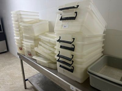 Plusieurs récipients en plastique sont empilés sur une table en métal dans une pièce.