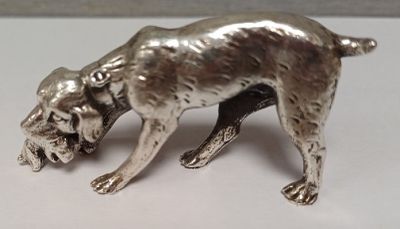 une figurine en argent représentant un chien, posée sur un fond blanc