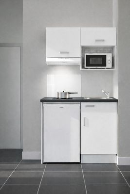 une petite cuisine avec des placards blancs et des plans de travail noirs