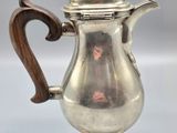 an antique silver coffee pot with a wooden handle on a white surface