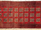 Un vieux tapis rouge à motifs est accroché à une clôture grillagée.