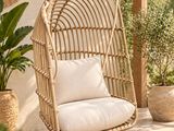 une chaise suspendue en rotin sur une terrasse agrémentée de plantes et de plantes en pot