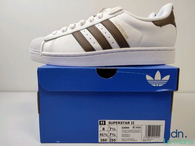 Des baskets adidas Superstar II blanches et marron posées sur une boîte bleue