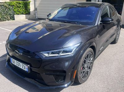 2020 ford mustang macht in a parking lot in front of a garage